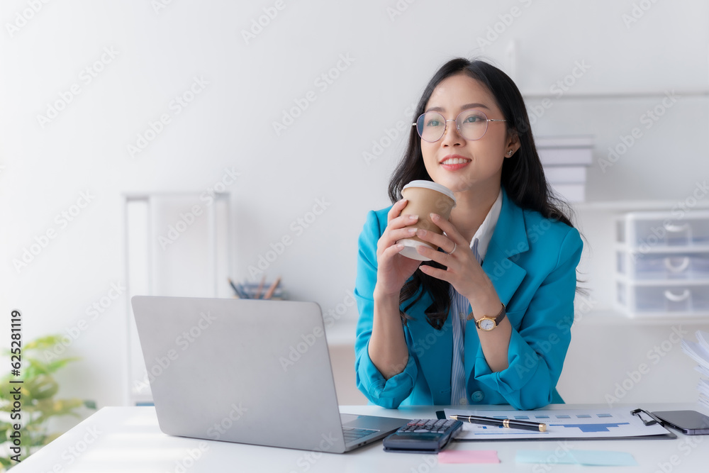Successful Asian businesswoman smiling using laptop computer and holding coffee cup at office. Confident Asia businesswoman sitting happily in the office. Successful Asian businesswoman smiling using laptop computer and holding coffee cup at office. Confident Asia businesswoman sitting happily in the office.