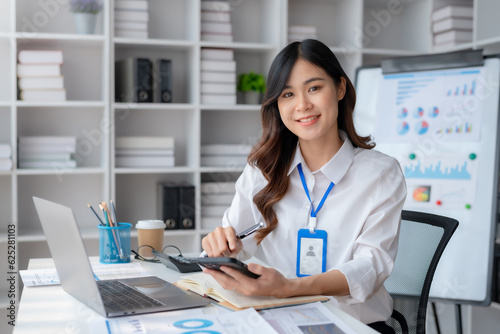 Portrait of a smiling asian businesswoman using mobile phone in the office. Young Asian businesswoman with paperwork at workplace using smartphone in a modern office.