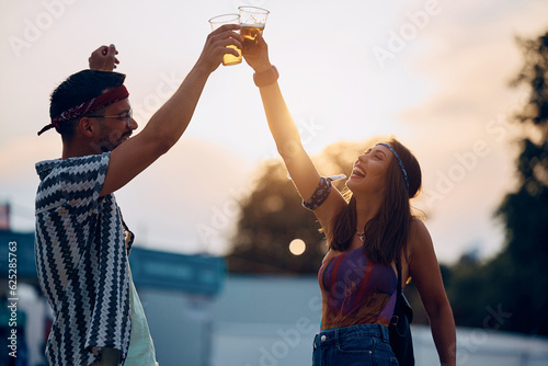 Carefree couple toasting with beer while having fun on summer music festival at sunset. © Drazen