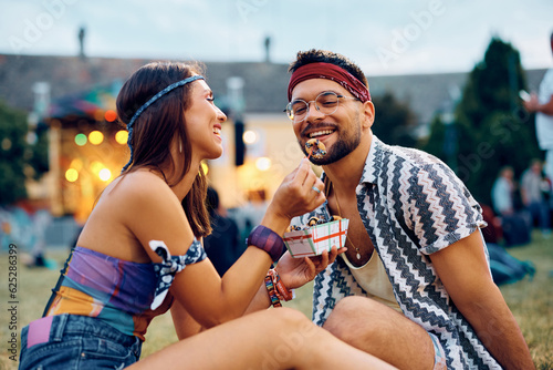 Happy woman feeds her boyfriend with mini donuts at open air music concert.