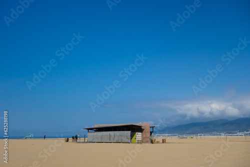 Views of Venice Beach in Los Angeles on a sunny summer day. Large sandy beach, waves, ocean, palm trees. © Adam