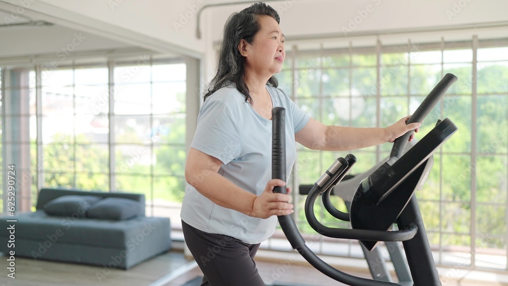 Asian elderly women exercising on the machine in living room at home. Mature woman enjoy doing exercising on treadmill for well being slimming weight. Elderly lifestyle concept Asian elderly women exercising on the machine in living room at home. Mature woman enjoy doing exercising on treadmill for well being slimming weight. Elderly lifestyle concept