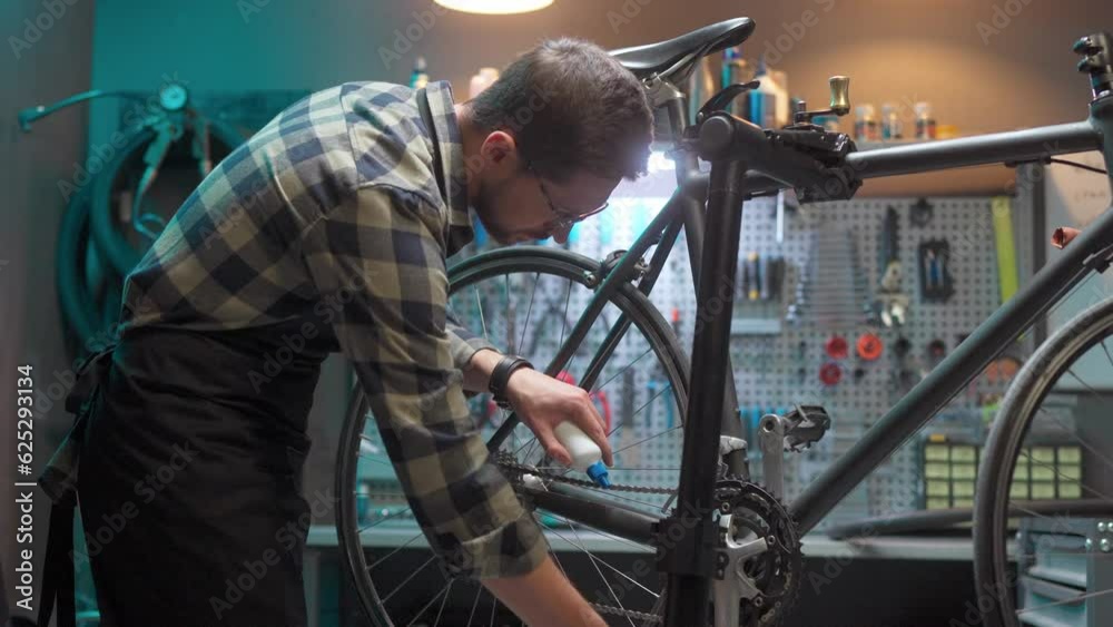 Craftsman repairing bicycle in workshop. Cycling mechanic in glasses and protective apron. Male on background of tools fixing bicycle pedals. Busy man at workplace in repair shop. Craftsman repairing bicycle in workshop. Cycling mechanic in glasses and protective apron. Male on background of tools fixing bicycle pedals. Busy man at workplace in repair shop.