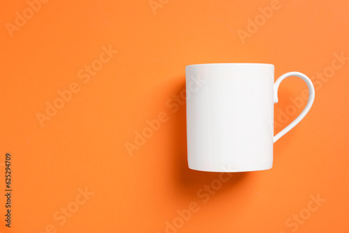 One white ceramic mug on orange background, top view. Space for text