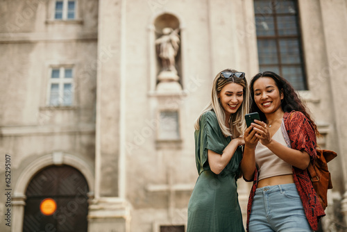 Smiling young females using a phone while walking through a city street while on vacation © La Famiglia