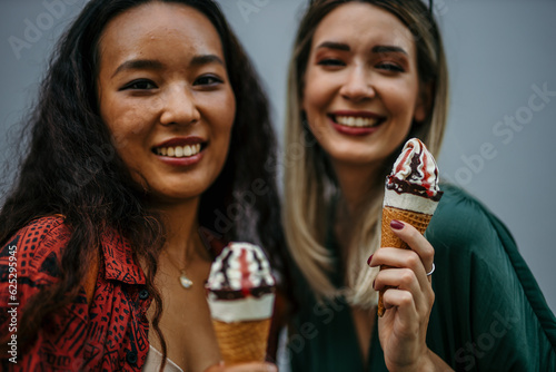 Two multiracial happy women having conversations and eating ice cream outdoors - Friendship and summer vacation concept