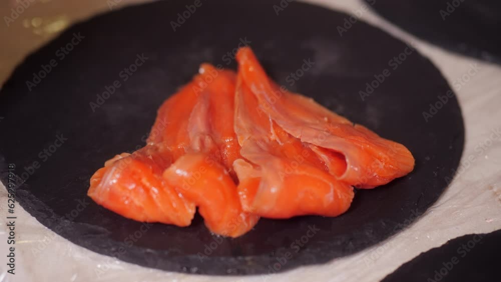Woman cook chef in gloves serving dish with fillet of salmon red fish on black wooden board in cafe. Catering service, preparing food in restaurant. Healthy products, nutrition, mediterranean diet.