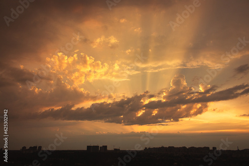 Dramatic evening sky with rays of light over city. Aerial view above cityscape in the dusk. Heaven concept. Sunshine in the sky. Sunset scenic sky. Sun rays through the clouds.