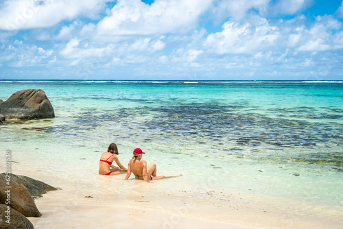 Two women on a paradise tropical beach with palm trees and turquoise water. Mahe Island  Seychelles. Anse Forbans Beach