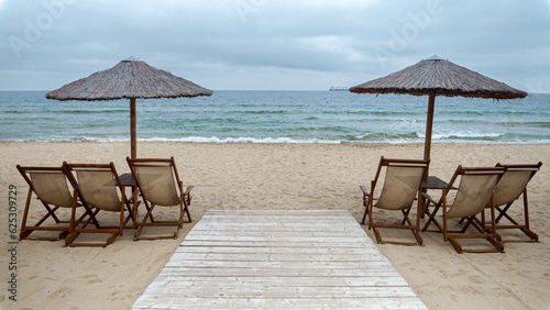 Empty wooden sunbeds and sun umbrellas on deserted beach on cold cloudy day. End of seasonal tourism, travel in winter.