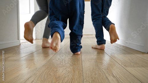 Two boys and their mother running on the wooden floor at home. Family happiness, playing together, and love.