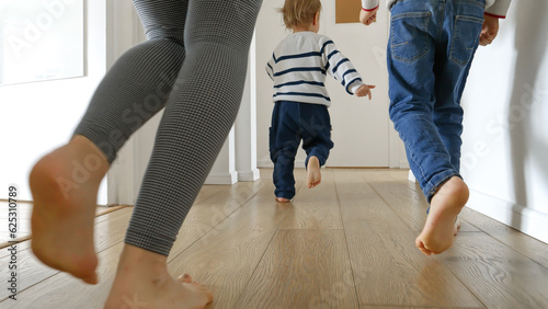 Closeup of mother and two boys running on the wooden floor at home. Concept of family love, joy, and fun in a household