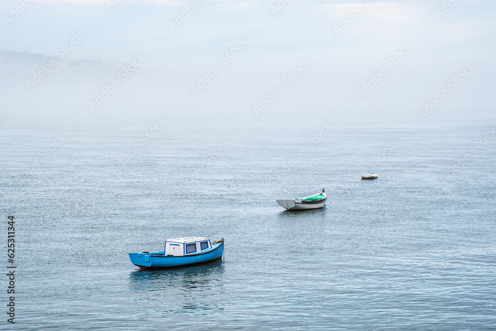 Boats in river on misty morning with background with heavy fog. Lisbon, Portugal
