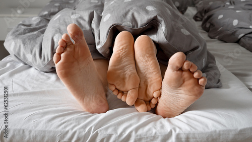Konstfotografi Couple's feet entangled under a blanket on a soft bed, showcasing the love and intimacy between them