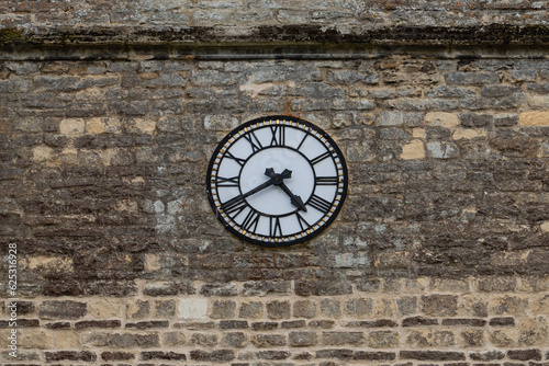 Vintage stone wall with real clock, white dial, black sword-shaped hands, Roman numerals. Weathered texture, time reads 4:40. Timepiece, classic design, historic, antique