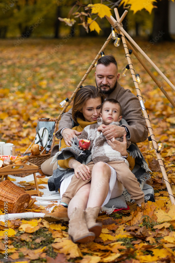 Happy family on a beautiful fall picnic in the park. Cozy autumn vibes. Young father, mother and their cute son spending quality time together, having fun. in the park Happy family on a beautiful fall picnic in the park. Cozy autumn vibes. Young father, mother and their cute son spending quality time together, having fun. in the park