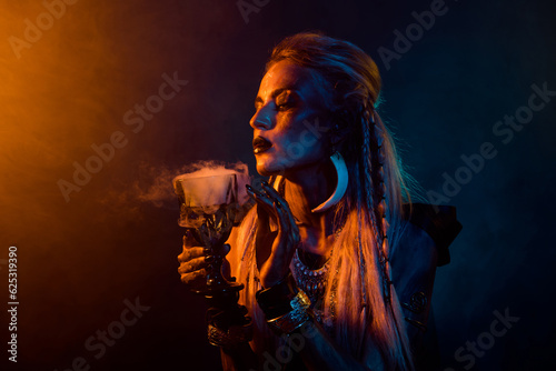 Photos Portrait of demonic pagan wizard girl hold smell potion cup orange light foggy m