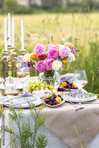 Summer sunset, romantic date outdoors in meadow, marriage proposal. Romantic sunset dinner in the field. Table honeymoon set for two with luxurious food, glasses of champagne drinks in a restaurant. 