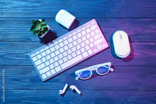 Keyboard, eyeglasses, computer mouse, earphones and houseplant on dark wooden background photo