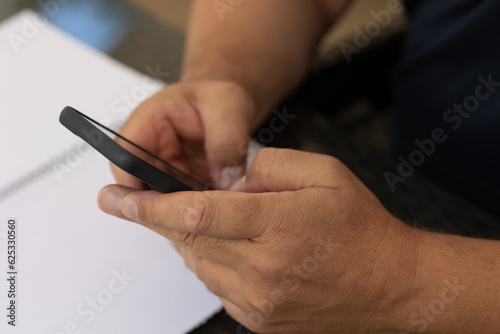 hands of a man typing on a telephone with a sheet of paper on the table