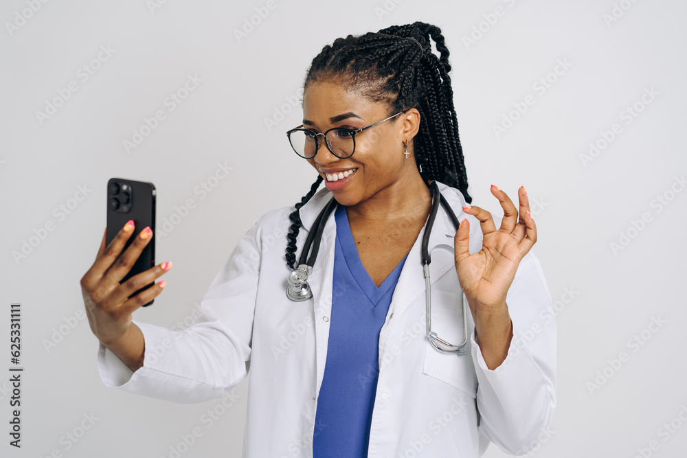 Portrait of happy african american nurse or doctor woman wearing medical lab coat holding and using cellphone isolated against white background Portrait of happy african american nurse or doctor woman wearing medical lab coat holding and using cellphone isolated against white background