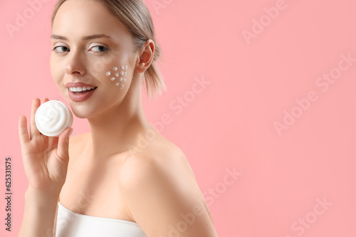 Pretty young woman with cream on her face against pink background