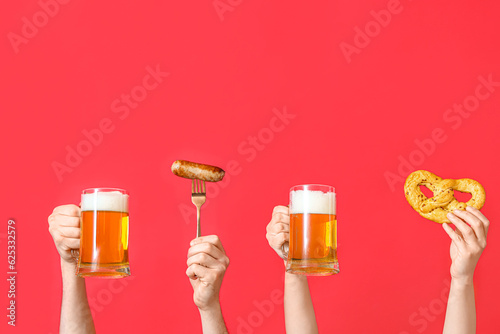 Many hands with mugs of cold beer, sausage and pretzel on red background