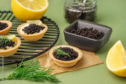 Grid of tasty tartlets with black caviar on green background