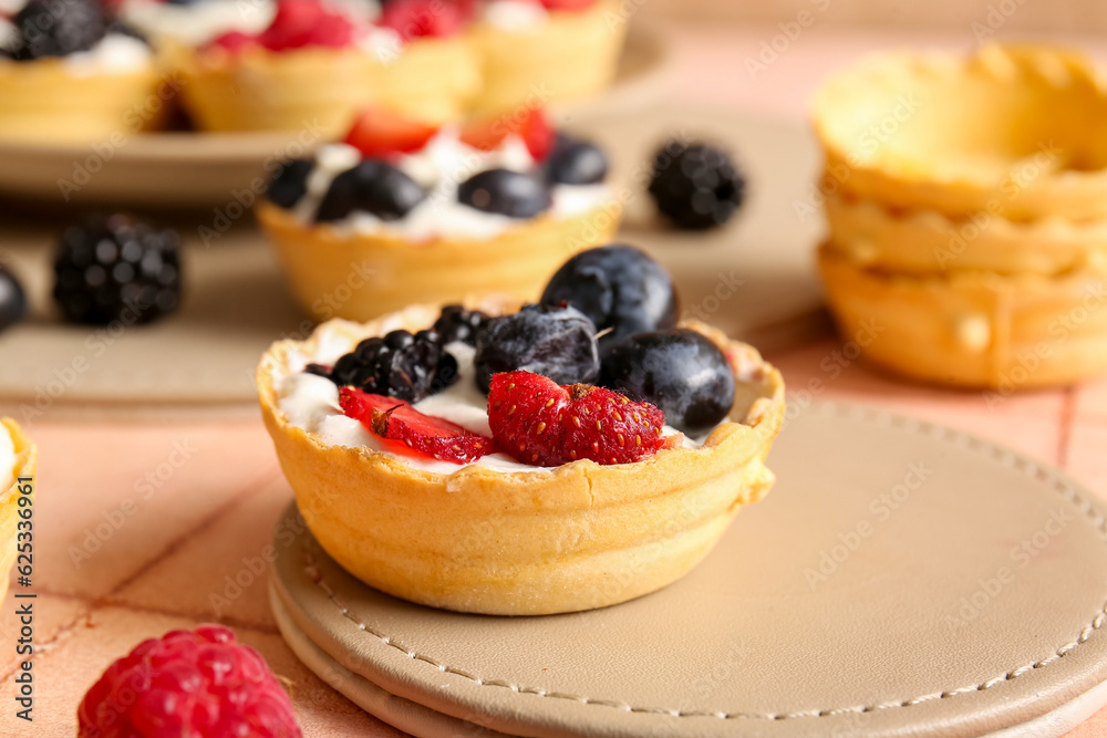 Tasty tartlets with whipped cream and berries on pink tile background Tasty tartlets with whipped cream and berries on pink tile background