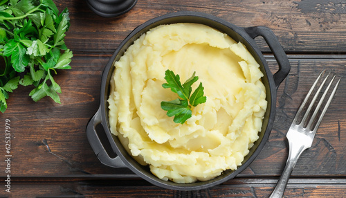 Fotografie Mashed potatoes or boiled puree with parsley in cast iron pot on dark wooden rustic background