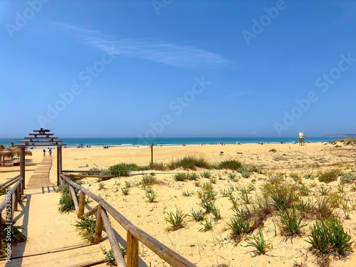 Wooden walkway to the wide sandy beach and dunes in Zahara de los Atunes on a beautiful summer day and blue sky, Playa del Cabo de la Plata, Andalusia, Cadiz Province, Spain