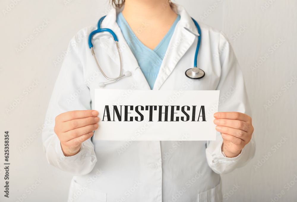 Female doctor holding paper with word ANESTHESIA on light background, closeup Female doctor holding paper with word ANESTHESIA on light background, closeup