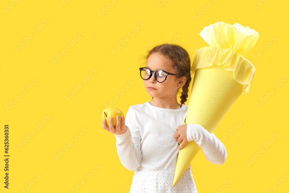 Happy little girl in eyeglasses with school cone and fresh apple on yellow background Happy little girl in eyeglasses with school cone and fresh apple on yellow background