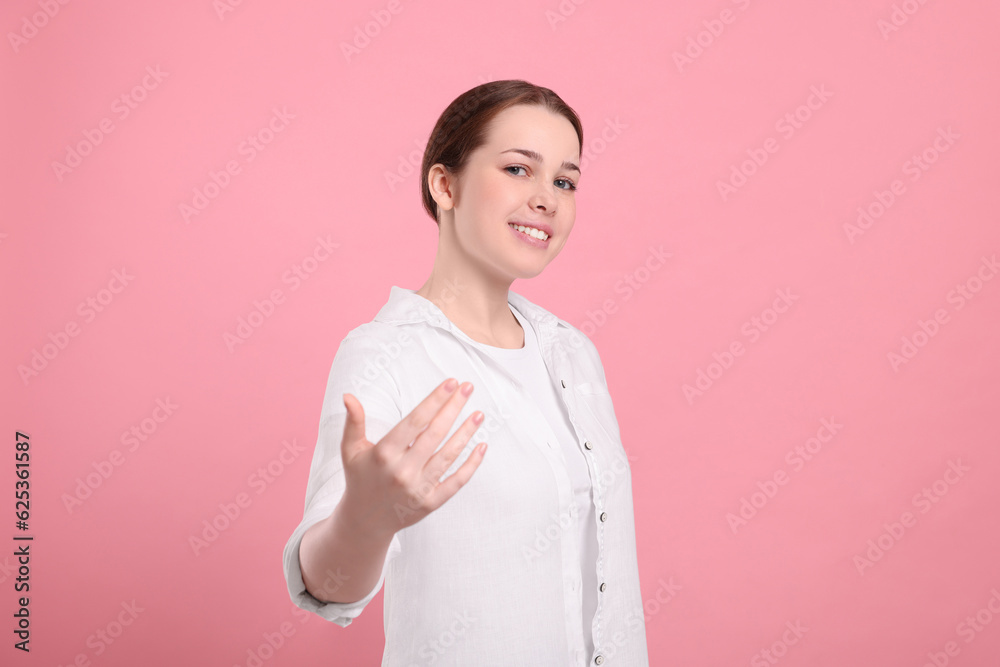 Happy woman inviting to come in against pink background Happy woman inviting to come in against pink background