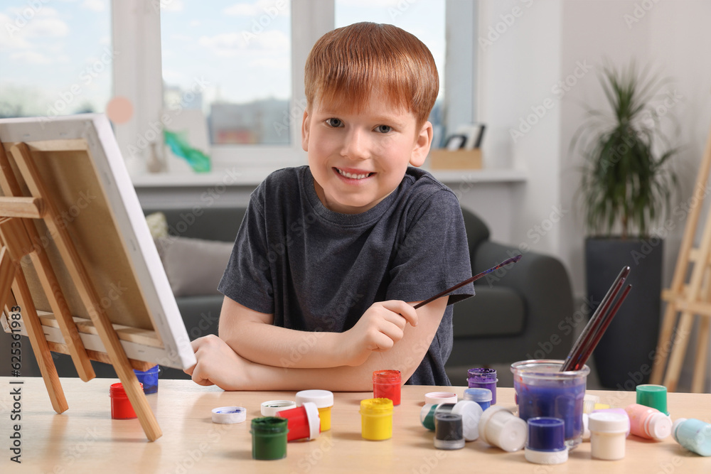 Happy little boy painting at table in studio. Using easel to hold canvas Happy little boy painting at table in studio. Using easel to hold canvas