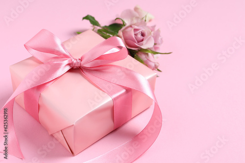 Gift box and beautiful rose flowers on pink background, closeup