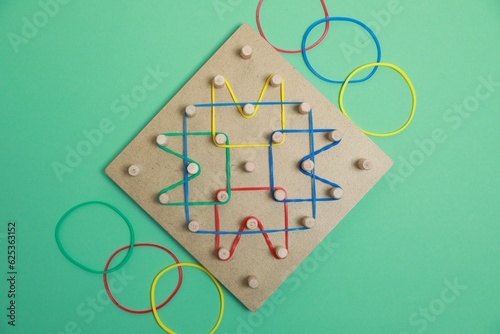 Wooden geoboard with rubber bands on green background, flat lay. Educational toy for motor skills development photo