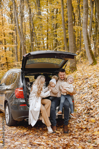 Young family sitting at open trunk of hatchback car in autumn forest © prostooleh