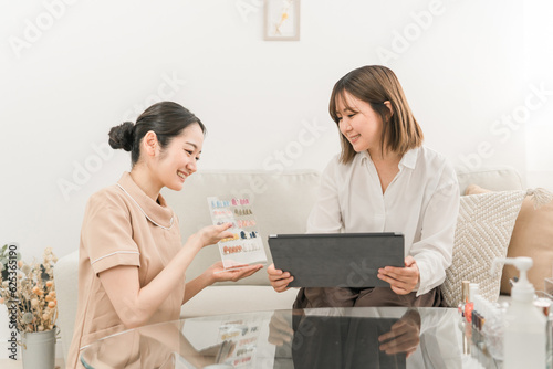 ネイルサロンでネイルチップを見ながらネイリストにカウンセリングを受ける日本人女性 