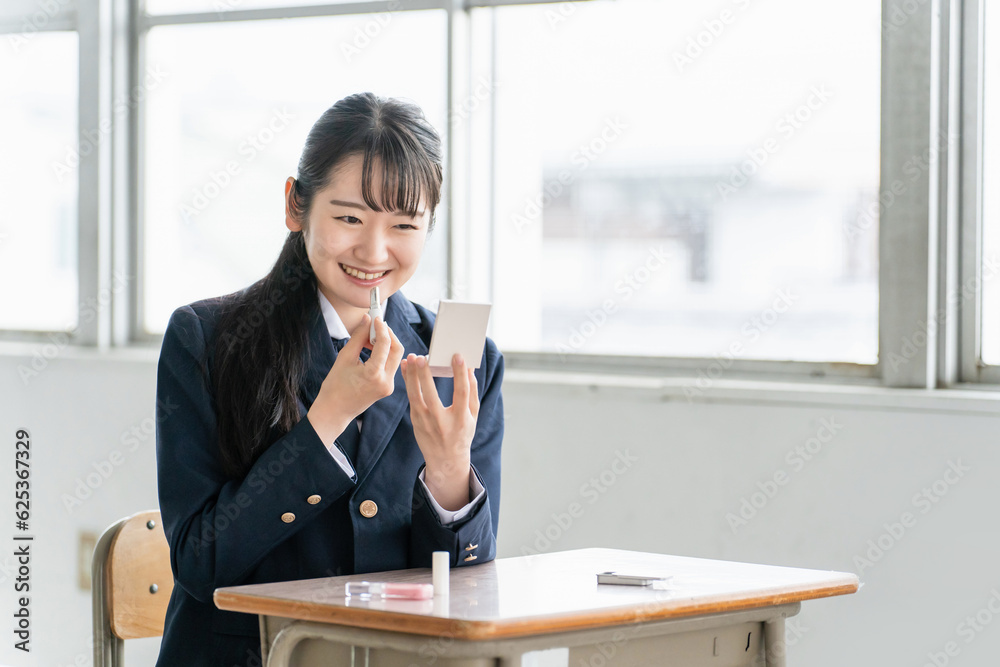 放課後に学校の教室で鏡を見ながらメイクをする笑顔の女子高生（リップ・口紅）
