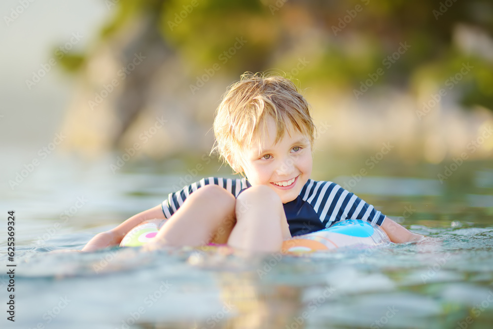 Little boy swimming with colorful floating ring in sea on sunny summer day. Cute child playing in clean water. Family and kids resort holiday during summer vacations.