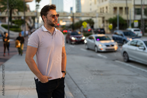 Man model in fashion in stylish polo walking on the city. Guy walks on the street. Urban fashion man in city walking street. Portrait of stylish handsome man outdoors. Portrait of attractive man