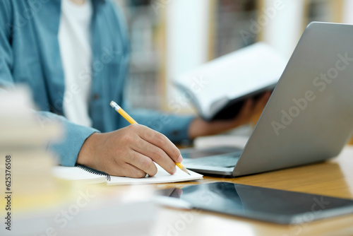 Young university student using laptop for online learning, searching and learning at library.
