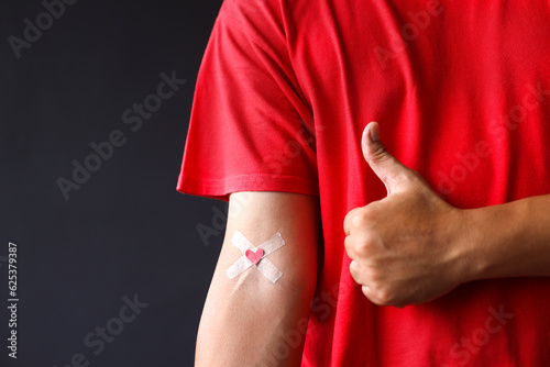 Leinwand Poster Man showing thumbs up near hand with plasters heart after giving blood