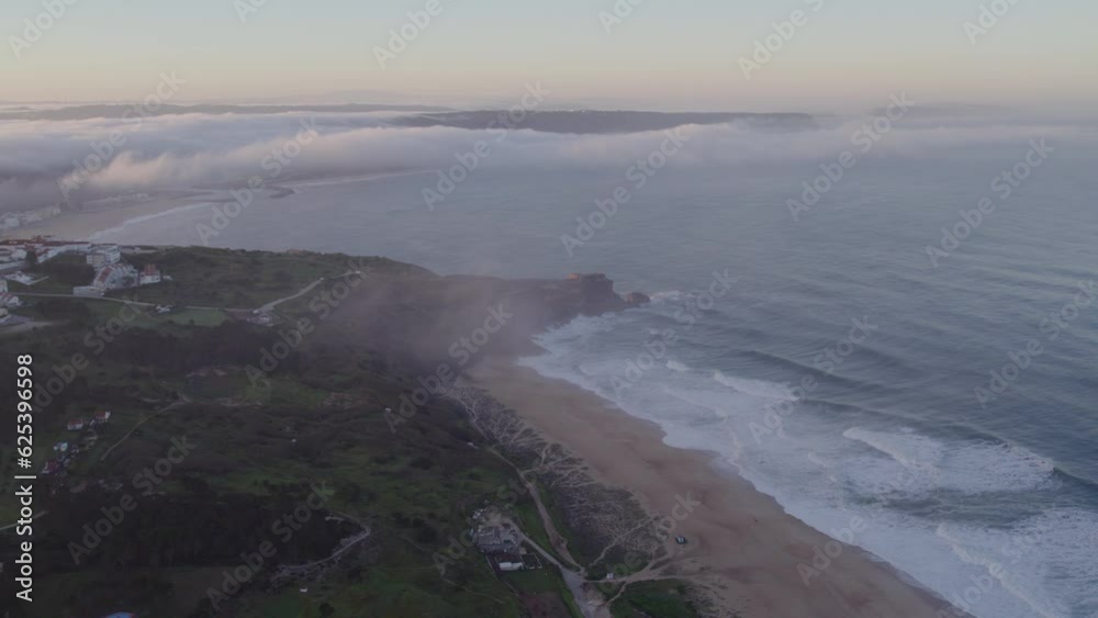 Drone view of Praia do Norte at Nazaré with low clouds during sunrise, aerial Drone view of Praia do Norte at Nazaré with low clouds during sunrise, aerial