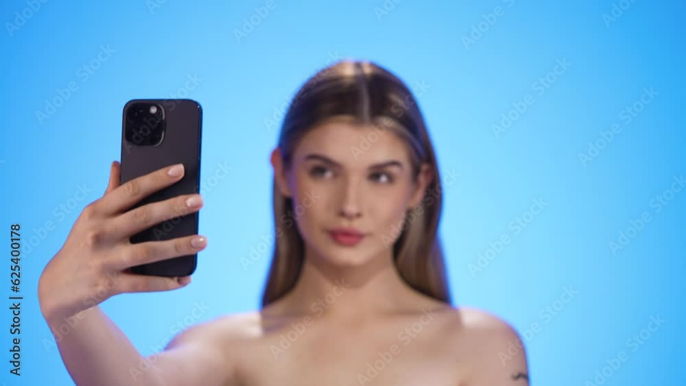 Rack focus selfie posing young woman to smartphone, isolated blue background Rack focus selfie posing young woman to smartphone, isolated blue background