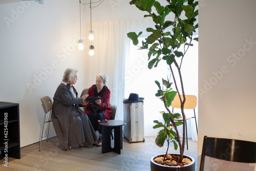 ホテルのロビーでタブレットを使うモダンな高齢女性たち © Monet