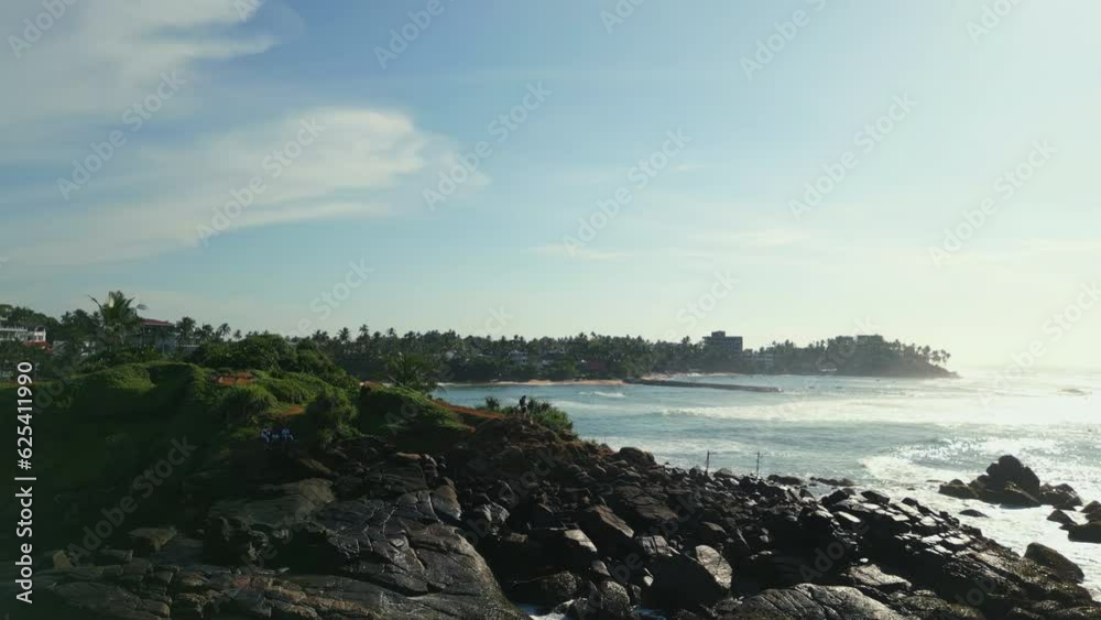 Young couple stands on top of green tropical rocky island in the middle of sea washed by waves aerial view. Scenic Parrot Rock in Mirissa, Sri Lanka surrounded by ocean down footage from a drone Young couple stands on top of green tropical rocky island in the middle of sea washed by waves aerial view. Scenic Parrot Rock in Mirissa, Sri Lanka surrounded by ocean down footage from a drone