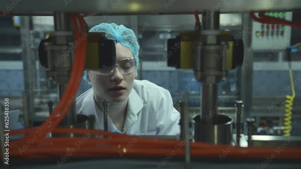 Female scientist in white coat and blue hat working in the control machine of production line. Female scientist in white coat and blue hat working in the control machine of production line.