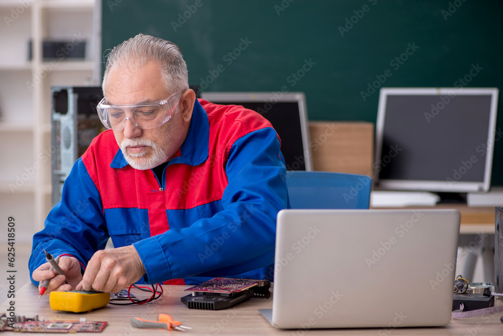 Old repairman repairing computers in the classroom Old repairman repairing computers in the classroom